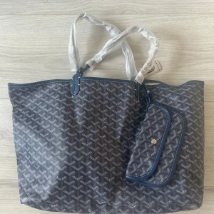 Blå handväska - Säljer en blå handväska med klassiskt grafiskt mönster och matchande avtagbar innerficka. Väskan har vita sömmar, blåa handtag och beige insida. Perfekt för dig som vill ha en ikonisk och rymlig väska med lyxig känsla. Hör av er vid minsta lilla fundering 