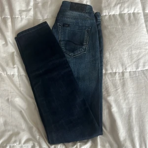 Mörkblå jeans från Lee X-Line W26 - Snygga mörkblå jeans från Lee X-Line. Jeansen har normal passform och raka ben. Tillverkade i slitstarkt denim. Perfekta för dig som gillar en tidlös look med lite edge.