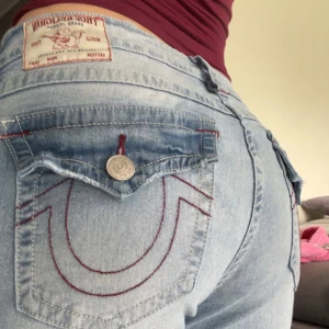 True Religion bootcut jeans - Säljer ett par ljusblå jeans från True Religion med ikoniska bakfickor och röd kontrastsöm. Köpta för 1299kr Mid waist. W30. Bootcut