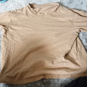 Beige basic t-shirt i bomull - Enkel och stilren beige t-shirt i mjuk bomull. Modellen är rak med korta ärmar och rund halsringning. Perfekt för en chill och avslappnad look, lätt att matcha med jeans eller shorts.