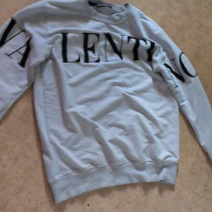 Vit sweatshirt från Valentino, storlek L - Säljer en vit sweatshirt från Valentino med stora svarta bokstäver över bröstet och ärmarna. Tröjan har rund halsringning och långa ärmar. Tillverkad i mjuk bomull, perfekt för en clean och stilren look.