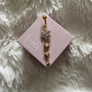 Lång navelpercing med blommor - Jätte snygg guldig lång navelpercing med blommor från india. Säljer då staven är för lång för mig och behöver en kortare stav. Använd 1 gång. 10cm lång stav. Rostfritt stål. 