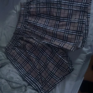 Rutig Burberry shorts size S - Snygga Burberry shorts i klassiskt beige, svart och vitt rutmönster. De har elastisk midja med snörning där Burberry-loggan syns, samt broderad logga på benet. Tillverkade i polyester med meshfoder, perfekta för sommaren eller stranden.