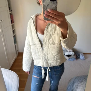 Quiltad beige/vit jacka från Zara - Säljer en quiltad beige/vit jacka från Zara i storlek S. Jackan har dragkedja framtill, två stora fickor och snörning i midjan. Den är lätt vadderad och har en loose passform med lång ärm. Jackan är ny och kommer i original förpackning. 