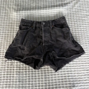 Svarta high waist jeansshorts &Denim - Svarta high waist jeansshorts från &Denim med råa, fransiga benslut och klassisk femficksdesign. Knappar i gylfen och bälteshällor. Perfekta för en avslappnad och cool look under varma dagar.