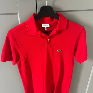 Röd pikétröja från Lacoste - Röd piké Lacoste säljer jag pga av att jag inte använder den. Använd mindre än 3 gånger. Den är som helt ny inga hål. Storlek 176