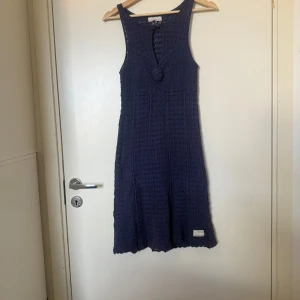Mörkblå virkad sommarklänning  - Supersöt mörkblå virkad klänning med ärmlös design och knyt-detalj framtill. Perfekt flowy passform och snygg struktur i materialet. Lätt och luftig, perfekt för varma dagar. Från märket Odd Molly i storlek 1 som ungefär motsvarar en storlek S. Fint skick, men den är blekare än ny. Och kan vara något tvätt påverkad. 