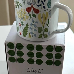Emalj mugg  - mugg med färgglada blommönster och en kartong med gröna blad samt texten 'Stig L.