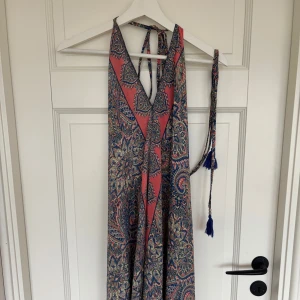 Mönstrad kortklänning - Snygg kortklänning från Addictive Tropezian Collection med paisleyinspirerat mönster i blått, rosa och beige. Klänningen har halterneck med knytband och dekorativa blå tofsar. Luftigt material, perfekt för varma dagar. Jag köpte den i samma butik som den gröna kjolen som ligge ruppe på min plick. Den är aldrig använd och har lappen kvar. Den har ingen storlek men passar mig som är xs/s