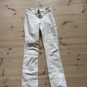 Vita bootcut jeans från Filippa K - Snygga vita jeans från Filippa K i bootcut-modell med hög midja. Byxorna har dragkedja och metallknappar. Tillverkade i mjuk bomull med lite stretch för extra komfort.