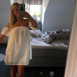 Vit offshoulder kortklänning med broderi - Superfin vit kortklänning med offshoulder och broderade detaljer. Klänningen har vida ärmar och ett luftigt, rakt fall. Perfekt till sommaren med sitt tunna bomullstyg och snygga broderade mönster. Söt och trendig stil som passar till många tillfällen.