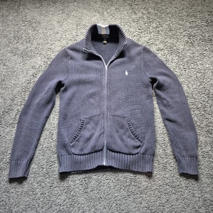 Mörkblå full-zip sweater från Polo Ralph Lauren - Säljer en mörkblå stickad full-zip sweater från Polo Ralph Lauren med  och två fickor och en vit, ljusblå rand på nacken. Klassisk broderad logga på bröstet och ribbade muddar vid ärmslut och nederkant. Väldigt skön och stilig tröja, och passar med de mesta. Priset kan alltid diskuteras😁