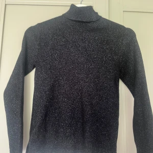 Glittrig svart polotröja från Zara - Snygg svart polotröja från Zara med glittriga inslag. Tröjan har lång ärm och en klassisk polokrage. Perfekt för dig som vill sticka ut lite extra med en stilren men ändå festlig look. Materialet är stretchigt och sitter skönt på kroppen. Ni ser att det är barnstorlek men tröjan passar mig som har xs/s