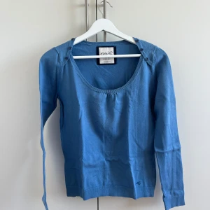 Blå långärmad tröja Esprit - Snygg blå långärmad tröja från Esprit med rundad halsringning och knappar på axlarna. Tröjan är i mjuk bomull och har en enkel, stilren design med liten logga nertill. Perfekt för dig som gillar en klassisk look med en twist.