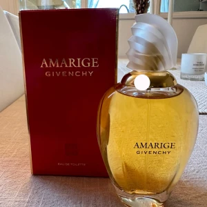 Givenchy Amarige Eau de Toilette 100ml - Givenchy Amarige Eau de Toilette i en elegant, kurvig glasflaska med guldig vätska och en unik vit, snirklig kork. Kommer i en lyxig röd kartong med gulddetaljer. Klassisk och feminin doft med exklusiv känsla.