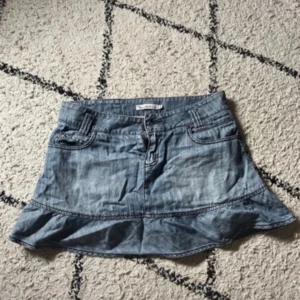 Jeanskjol med volang från bondelid - Supersöt ljusblå jeanskjol från Bondelid med volang nertill. Klassisk femficksmodell framtill och snygga detaljer bak. 