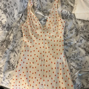 Vit kortklänning med jordgubbsmönster Zara - Supersöt vit kortklänning från Zara med små röda jordgubbar över hela tyget. Klänningen har djup v-ringning, är ärmlös och har en lätt utställd passform. Perfekt för sommardagar och picknickar. Storlek L men passar mig perfekt som brukar ha S/M🩷