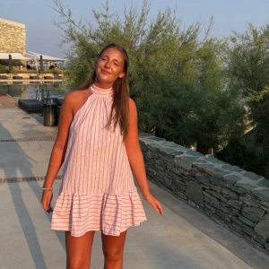 Ljusrosa randig kortklänning - Supersöt ljusrosa kortklänning med tunna vertikala ränder och volang nertill. Klänningen har hög hals och är ärmlös, perfekt för varma dagar. Den har en luftig och loose passform som ger en chill vibe.