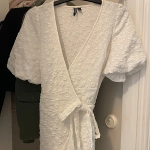 Vit omlottklänning med volang - Superfin vit kort omlottklänning med puffärmar och knyt i midjan. Storlek xs knappt använd❣️perfekt studentklänning 