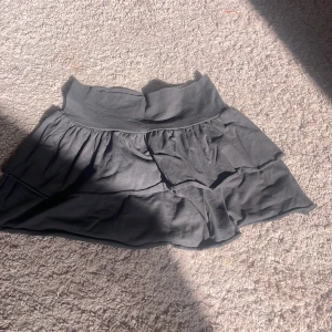 Svart volangkjol från H&M - Svart kortkjol från H&M med bred resår i midjan och dubbla volanger som ger en snygg och flowy look. Kjolen är gjord i mjuk bomull och passar perfekt till sneakers eller boots för en chill vibe.