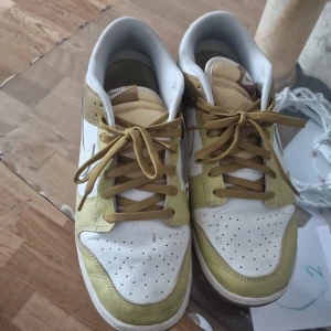 Nike Dunk sneakers i vitt och olivgrönt - Nike Dunk sneakers med lågt skaft i vitt och olivgrönt skinn. Klassisk siluett med perforerad tå, bruna snören och vit swoosh på sidan. Yttersulan är i gummi med tydligt Nike-mönster. Perfekta för dig som gillar streetstyle och vill sticka ut. Vi kan rengöra skorna inan dem blir köpta. Dem är köpta från Nike factory för 800.