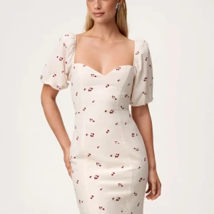 Vit Adooreklänning med puffärm och öppen rygg - Superfin vit långklänning med små röda blommor, puffärmar och markerad midja. Klänningen har öppen rygg med knyt och slits bak. Söt och romantisk look med mjukt fallande material och smickrande ringning framtill. Använd endast en gång. Nyskick. Ord pris 1695kr