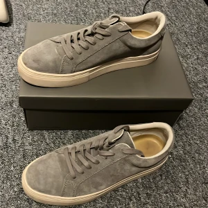 Grå mockasneakers från Vagabond - Snygga grå sneakers från Vagabond i mjuk mocka med klassisk rund tå och platt vit sula. Skorna har snörning och stilren design som passar till det mesta. Perfekta för dig som gillar en clean och modern look.