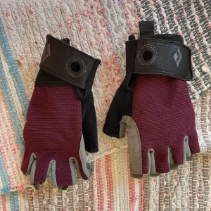 Träningshandskar från Black Diamond - Säljer ett par fingerlösa träningshandskar från Black Diamond. De har vinröd ovansida, svarta detaljer och grå mockaliknande handflator. Justerbar kardborre vid handleden och förstärkta greppytor. Perfekta för gym eller klättring. Storlek S. Köpta för 250kr. Använda endast en gång. 