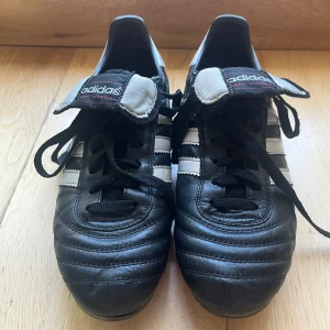 Adidas Copa Mundial fotbollsskor svart/vit - Klassiska Adidas Copa Mundial fotbollsskor i svart skinn med vita detaljer och de ikoniska tre ränderna på sidorna. Skorna har snörning, platt sula med fasta dobbar med Adidas-logga. Har använts ganska mycket men är fortfarande i super fint skick! 