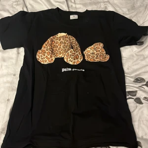 Palm Angels svart t-shirt med leopardnalle - Svart t-shirt från Palm Angels med ikoniskt tryck av en leopardmönstrad nalle på bröstet och vit logga under. Klassisk passform och korta ärmar, perfekt för dig som vill sticka ut med streetstyle-vibe.