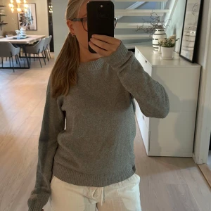 Grå stickad tröja med rund hals - Mysig grå stickad tröja med rund halsringning och långa ärmar. Tröjan har ribbade muddar vid ärmslut och nederkant, perfekt för lager-på-lager. Enkel och stilren design som funkar till allt.
