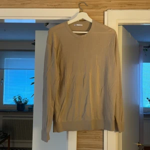 Beige långärmad tröja från Zara - En stilren beige långärmad tröja från Zara i storlek L. Tröjan har rund halsringning och är tillverkad i ett mjukt material som känns skönt mot huden. Perfekt för dig som gillar en clean och enkel look.