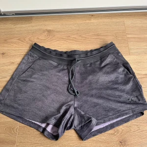 Grå träningsshorts från Kari Traa - Mörkgrå träningsshorts från Kari Traa med elastisk midja och snörning. Shortsen har en sportig look, sidofickor och är tillverkade i ett lätt och ventilerande syntetmaterial. Perfekta för gymmet eller löprundan.
