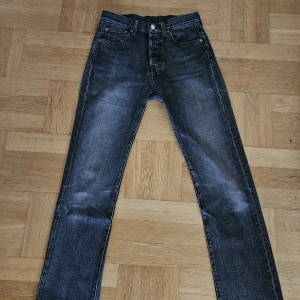 Levi's 501 gråa jeans W28 L32 - Snygga Levi's 501 Premium jeans tvättad denim med klassisk rak passform. Jeansen har fem fickor, knappgylf och coola slitningar för en vintagekänsla. 