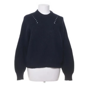 Mörkblå stickad tröja med håldetaljer - Mysig mörkblå stickad tröja med rund hals och diskreta håldetaljer vid axlarna. Tröjan har en loose passform och långa ärmar med ribbade muddar. Perfekt för lager-på-lager och chill dagar.