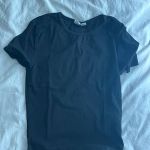 Svart basic t-shirt från Basically Basics - En svart, klassisk t-shirt från Basically Basics i storlek S. T-shirten har rund halsringning och korta ärmar, perfekt för en clean och enkel look. Tillverkad i mjuk bomull som känns skön mot huden. Passar dig som gillar minimalistisk stil.