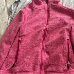 Rosa fleecejacka från Cross Sportswear - Säljer en riktigt skön rosa fleecejacka från Cross Sportswear. Jackan har hel dragkedja framtill, två fickor med dragkedja och hög krage. Perfekt för kyliga dagar och enkel att slänga på sig. Materialet är mjukt och värmande fleece.