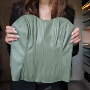 Grön korsett i skinnimitation - Snygg grön korsett med markerade sömmar och strapless design. Toppen är gjord i skinnimitation och har en figurnära passform som ger en cool och edgy look. Perfekt att styla med jeans eller kjol för en trendig outfit.