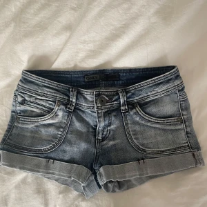 Blå jeansshorts från ONLY - Snygga blå jeansshorts från ONLY med klassisk femficksdesign och uppvikta benslut. Shortsen har normal passform, dragkedja och knapp framtill samt slitna detaljer för en cool look. Perfekta för varma dagar och enkel att matcha med allt.