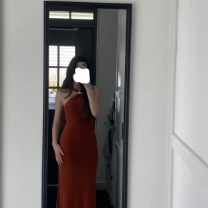 Rostbrun långklänning med öppen rygg - Snygg rostbrun långklänning med oneshoulder och twistad detalj framtill från Asos. Endast använd en gång. 
