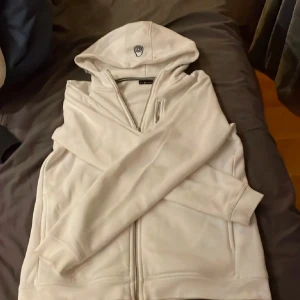 Vit zip hoodie från Sail Racing - Säljer en stilren vit hoodie från Sail Racing. Den har en dragkedja framtill och en praktisk huva. Fint skick! Kan tänka mig att sänka pris i snabb affär. Storlek 170 men passar även xs