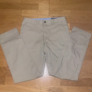 Beige chinos från Polo Ralph Lauren - Snygga beige chinos från Polo Ralph Lauren med klassisk rak passform. Byxorna har sidfickor, bakfickor med knappar och bälteshällor. Tillverkade i mjuk bomull som känns skön hela dagen. Perfekta för en clean och stilren look.