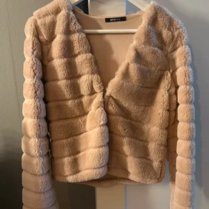 Rosa pälsjacka från Gina Tricot - Supermjuk och fluffig rosa pälsjacka från Gina Tricot med croppad passform och horisontella sömmar. Jackan har lång ärm och en öppen front som ger en trendig look. Perfekt för dig som vill sticka ut med en cozy vibe. STORLEK S