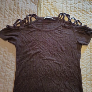 Svart ribbad topp med snörning FB Sister - Cool svart ribbad topp från FB Sister i storlek M. Toppen har korta ärmar och snygga snörningsdetaljer över axlarna som ger en unik look. Perfekt för dig som vill sticka ut med en edgy stil. Materialet är mjukt och stretchigt för en bekväm passform.