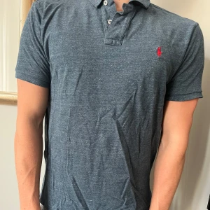 Mörkblå pikétröja från Ralph Lauren - Snygg mörkblå pikétröja från Ralph Lauren med klassisk krage och två knappar. Tröjan har korta ärmar och den ikoniska röda loggan broderad på bröstet. Tillverkad i mjuk bomull som känns skön mot huden. 8/10, storlek XL men passar som M. 