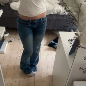 Blå bootcut jeans med broderade fickor - Säljer ett par blå bootcut jeans med låg midja och snygga broderade detaljer på bakfickorna. Från början är de högmidjade men har sytt om till lågmidjat.