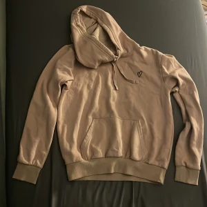 Beige hoodie med hjärtdetalj H&M Divided - Mysig beige hoodie från H&M Divided i storlek XS. Tröjan har en broderad hjärtdetalj på bröstet, känguruficka och huva med snörning. Perfekt för chill dagar och enkel att matcha med jeans eller leggings. Har ni några funderingar är det bara att skriva till mig på dm🩷
