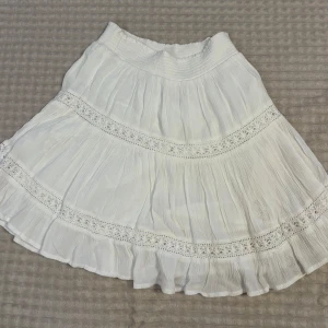 Vit kortkjol från Pull&Bear - Superfin vit kortkjol från Pull&Bear med  resår i midjan och snygga virkade spetsdetaljer. Knappt använd men den har märke från klistermärke som suttit på vid köptillfälle. Storlek s