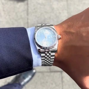 Silverfärgad Seiko automatisk klocka - Stilren Seiko klocka i silver med automatisk urverk. Klockan har en ljusblå urtavla med tydliga index och datumvisning. Länken är i klassisk stål och boetten har räfflad kant. Perfekt accessoar för dig som gillar en clean och elegant look.
