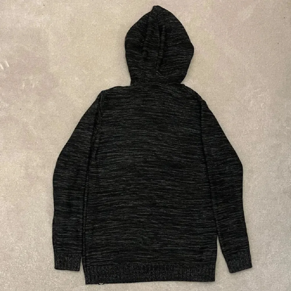 Säljer en svart stickad hoodie med en mysig känsla. Den har en praktisk ficka framtill och justerbar huva med snören. Perfekt för kyliga dagar.. Neuletakit & Villapaidat.